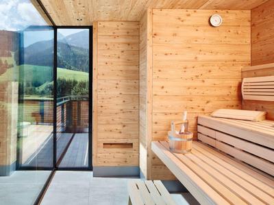 Moderne Holzsauna mit Bank, Glaswand und Blick auf grüne Landschaft.