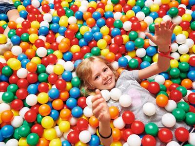 Kind liegt glücklich in einem Becken voller bunter Plastikbälle in Rot, Blau, Gelb und Weiß.