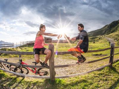 Zwei Radfahrer machen eine Pause und geben sich die Hand auf einem ländlichen Weg im Sonnenlicht.