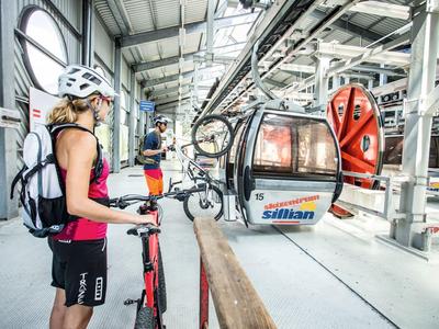 Person mit Helm und Rucksack wartet an einer Seilbahnstation in einer Halle.