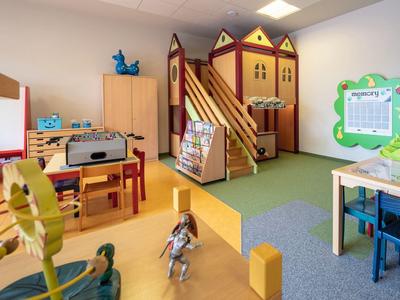 Kindergartenraum mit Spielhaus, Spielzeug, bunten Möbeln und Lernmaterialien in hellem Licht.