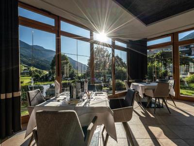 Helles Restaurant mit großen Fenstern, Tischen, Stühlen und Blick auf grüne Berge im Sonnenlicht.