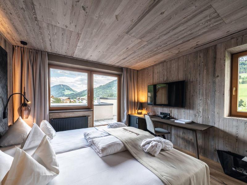 Modernes Schlafzimmer mit Holzwänden, großem Bett, Balkon und Fernseher, Blick auf Berge.