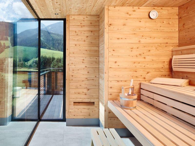 Moderne Holzsauna mit Bank, Glaswand und Blick auf grüne Landschaft.