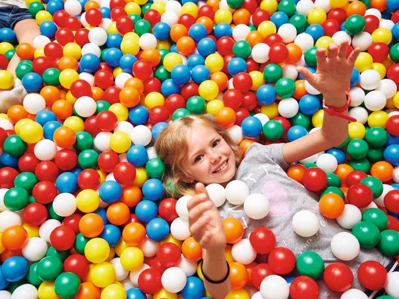 Kind liegt glücklich in einem Becken voller bunter Plastikbälle in Rot, Blau, Gelb und Weiß.
