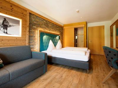 Gemütliches Hotelzimmer mit Doppelbett, Sofa, Schreibtisch und moderner Holzeinrichtung.