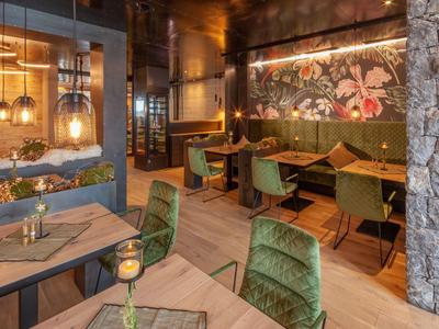 Gemütlicher Hotelrestaurantbereich mit grünen Stühlen, Holztischen und dekorativer Wandbeleuchtung.