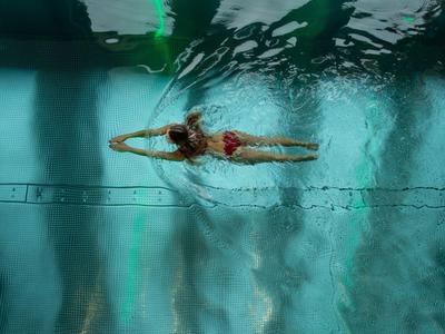 Eine Person schwimmt auf dem Rücken in einem blauen Hallenbad mit Wasserreflexionen.
