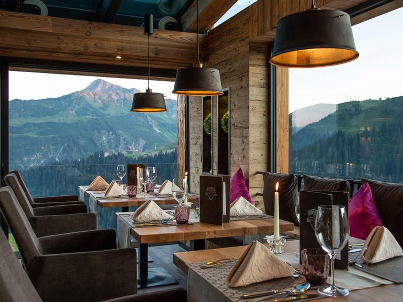 Gemütliches Restaurant mit Holzwänden, großen Fenstern und Bergblick, gedeckte Tische mit Wein.