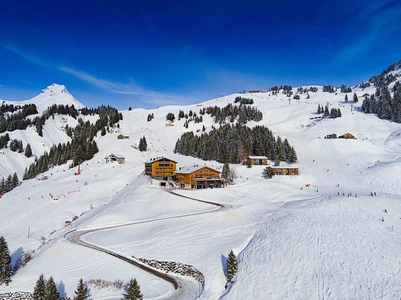 Schneebedeckte Alpenlandschaft mit Bauernhäusern, Bäumen und blauem Himmel.