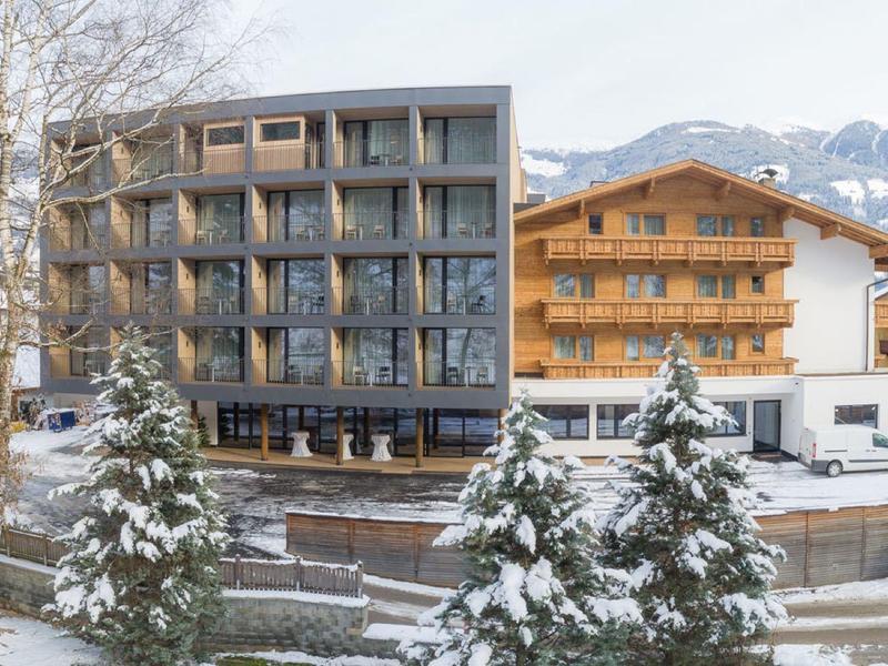Zwei nebeneinanderstehende Gebäude, eines modern mit Glas und Holz, das andere traditionell aus Holz, umgeben von Schnee.