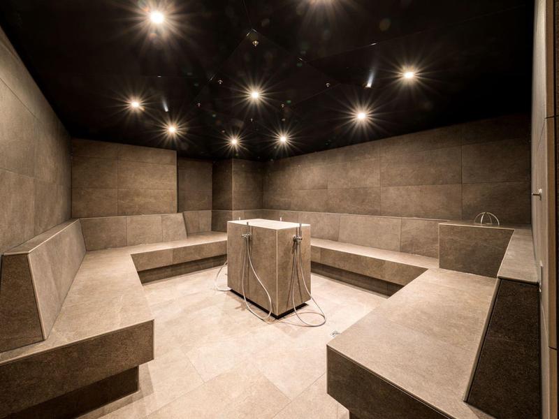 Moderner Ruheraum mit grauen Betonbänken und zentralem Tisch, dunkler Decke und Warmlichtlampen.