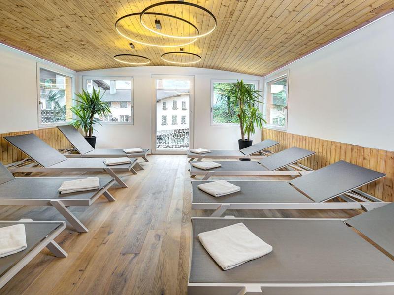 Ruheraum mit Liegen, Holzboden und Holzdecke, großen Fenstern und Zimmerpflanzen.