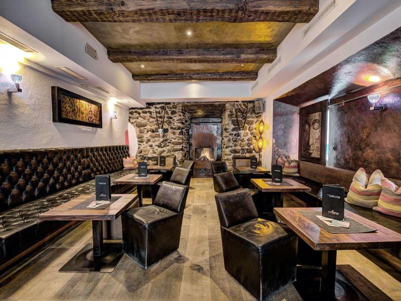 Gemütlicher Gastraum mit Holzbalken, Steinwand, Lederstühlen und dunklen Holztischen.