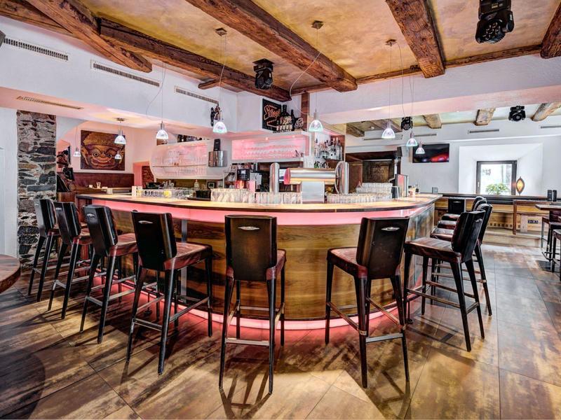 Modern eingerichtete Bar mit Holzboden, Barschrank und schwarzen Barstühlen im warmen Licht.