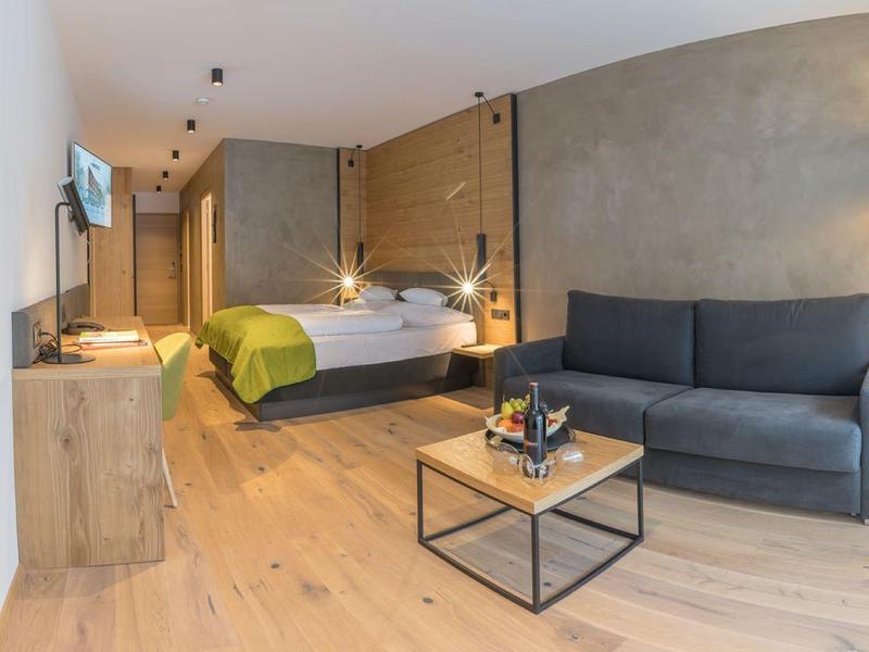 Modernes Hotelzimmer mit grauer Couch, Holzboden, Doppelbett und schlichtem Holzmöbel.