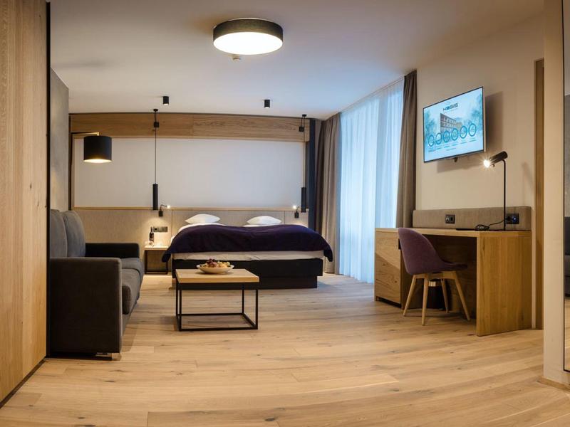 Moderner Hotelzimmer mit Doppelbett, Schreibtisch, Sofa, Fernseher und hellem Holzboden.