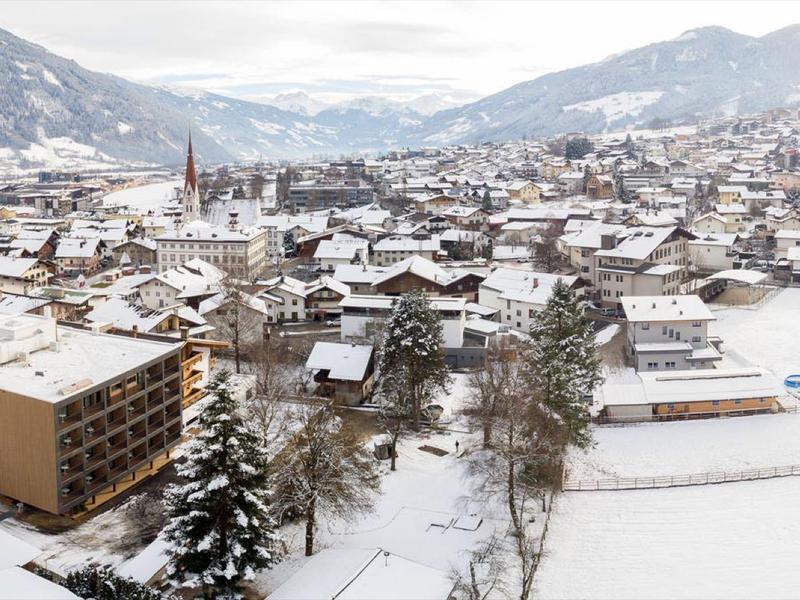 Verschneite Kleinstadt im Tal, umgeben von Bergen mit bewölktem Himmel und winterlicher Atmosphäre.