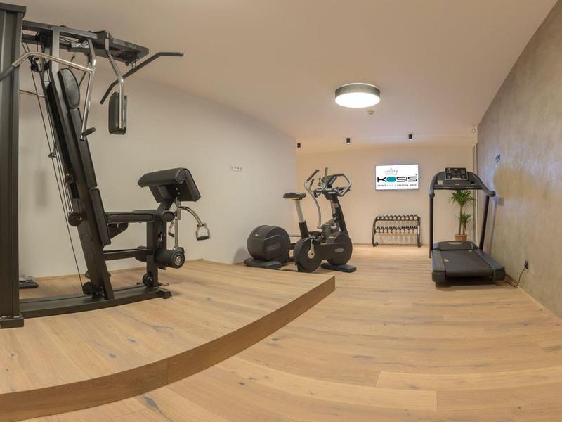 Kleiner Fitnessraum mit hellen Holzböden, Betonwand und verschiedenen Trainingsgeräten.