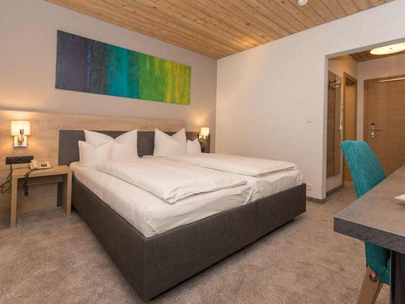 Modernes Schlafzimmer mit großem Doppelbett, Holzdecke, Teppichboden und buntem Wandbild.