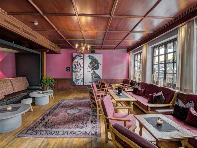 Gemütlicher Lounge-Bereich mit Holzboden, rosa Wänden, Sitzgruppen und großen Fenstern.