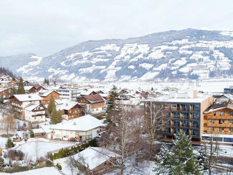 Winterlandschaft mit schneebedeckten Häusern, Hügeln und Bergen im Hintergrund.
