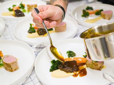 Ein Kellner gibt mit einem Löffel Soße auf ein kunstvoll angerichtetes Gericht in einem Restaurant.