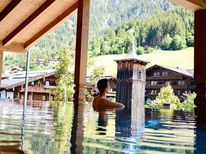 Person entspannt in einem überdachten Außenpool mit Blick auf Wald und Berge.