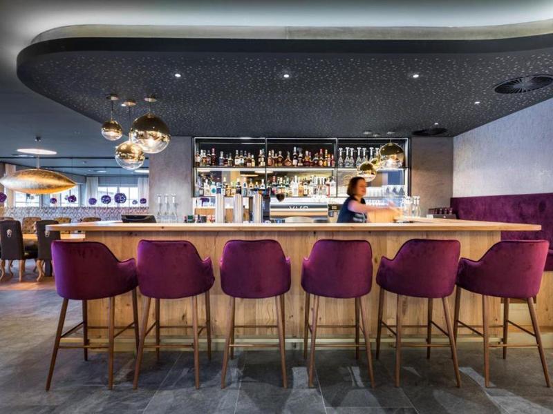 Moderne Hotelbar mit Holztresen, lila Barhockern und stilvoller Beleuchtung