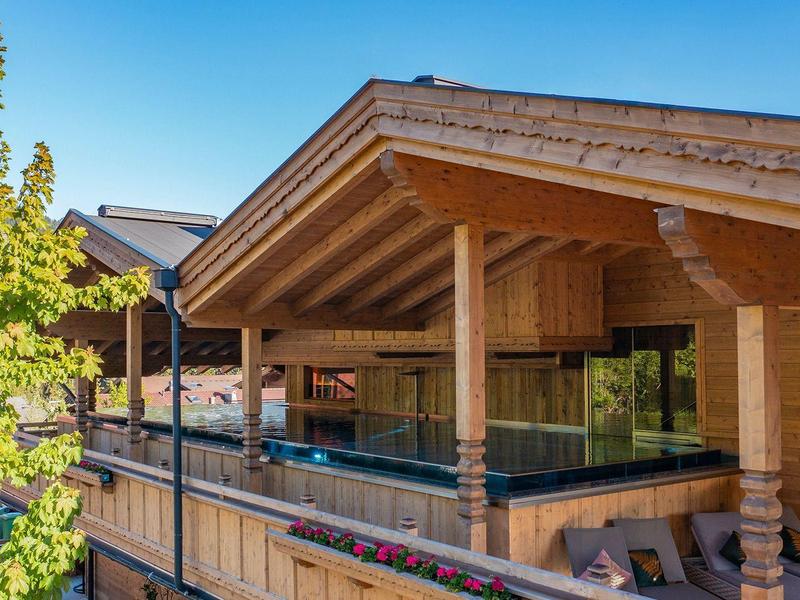 Moderner Holzbau mit großer Terrasse und Glaswänden unter blauem Himmel in bergiger Umgebung