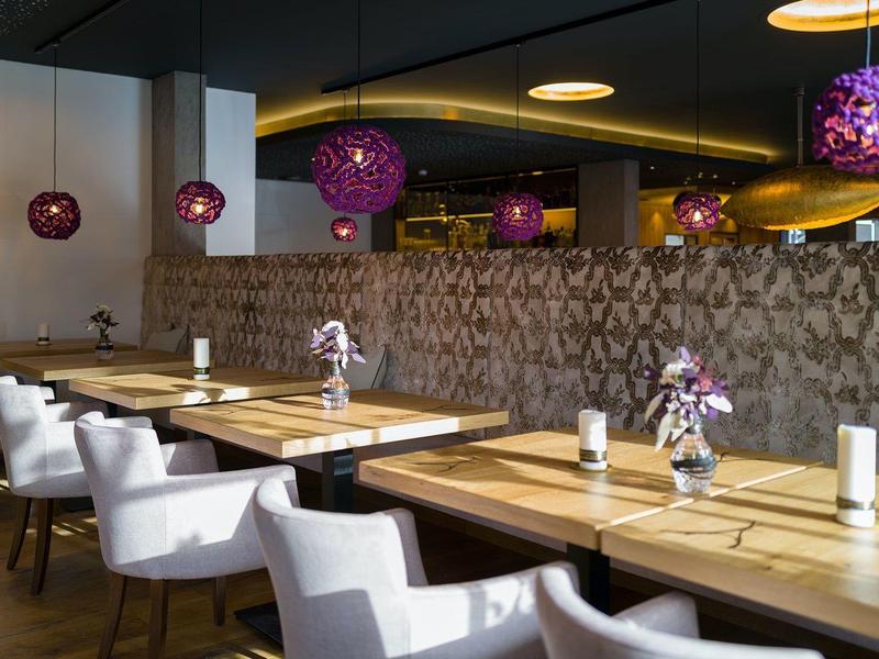 Modern eingerichteter Frühstücksbereich mit Holztischen, weißen Stühlen und violetten Lampen.