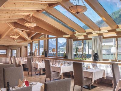 Licht restaurant met houten plafond, grote ramen en tafels met witte tafelkleden.