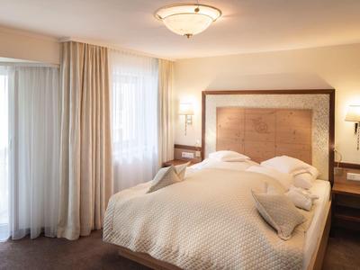 Cozy hotel room with large bed, white curtains, and warm lighting.