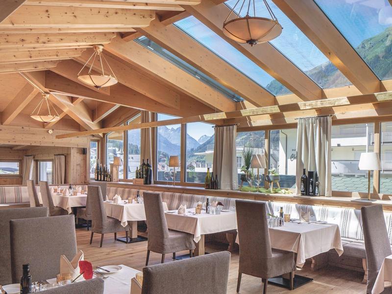 Bright restaurant with wooden beams, glass ceiling, and panoramic mountain and lake views.