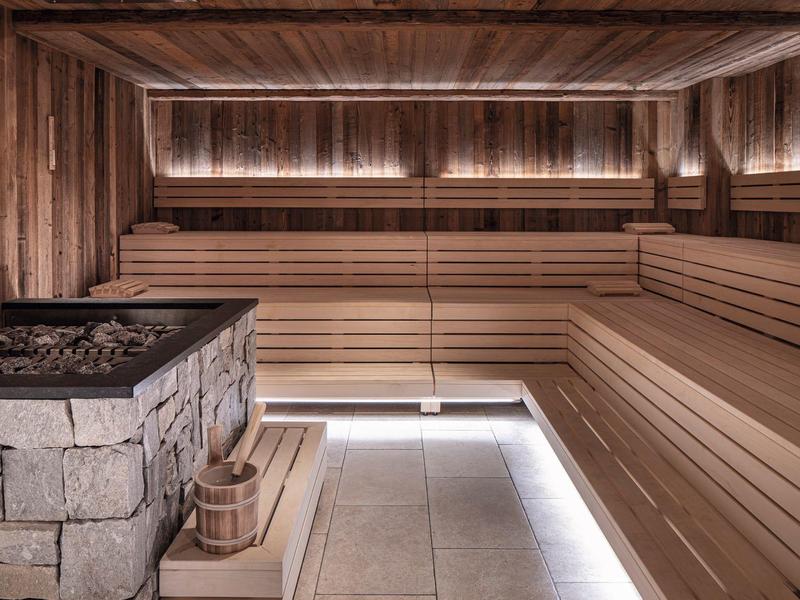 Modern sauna with wooden benches, stones, and soft LED lighting in warm tones.