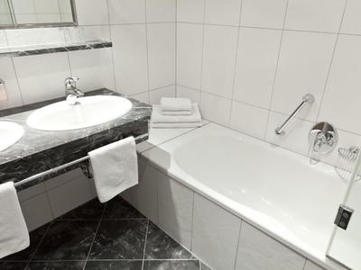 Helles Badezimmer mit weißer Badewanne, Marmorwaschbecken und dunklem Fliesenboden.