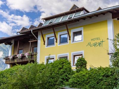 Gelbes Hotelgebäude mit Balkon, vielen Fenstern und grünen Sträuchern im Vordergrund.