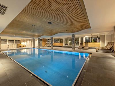 Moderner, innenliegender Swimmingpool mit Holzdecke, bequemen Liegestühlen und warmem Licht.