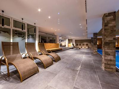 Moderner Wellnessbereich mit Liegen, großen Fenstern und Schwimmbecken in warmem Licht.