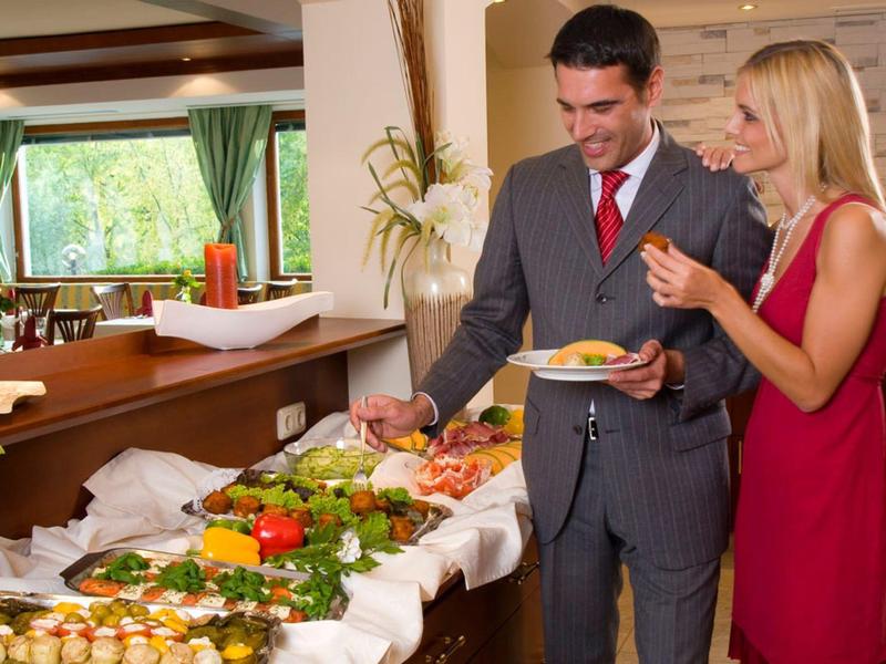 Ein Paar in eleganter Kleidung wählt Speisen an einem festlich dekorierten Buffet in einem Hotelrestaurant.