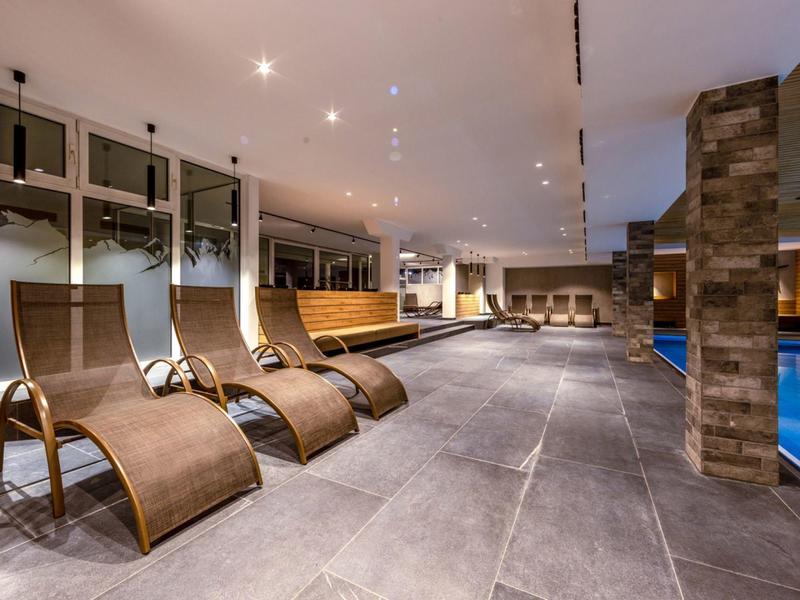 Moderner Wellnessbereich mit Liegen, großen Fenstern und Schwimmbecken in warmem Licht.