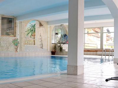 Helles Hallenbad mit Säulen, großen Fenstern und blau schimmerndem Wasser.