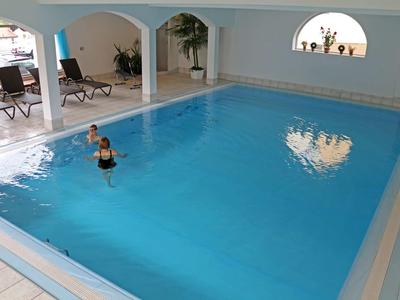 Innenpool mit klar blauem Wasser, zwei Personen im Wasser und Liegestühlen an der Seite.