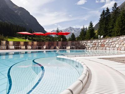 Außenpool mit klar blauem Wasser, rotem Sonnenschirm, umgeben von Bergen und grünen Bäumen.