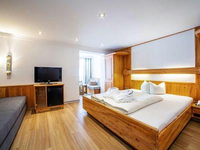 Helles Schlafzimmer mit Holzmöbeln, großem Bett, TV, Sofa und Holzfußboden.