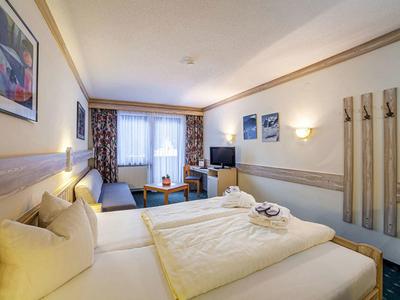 Gemütliches Hotelzimmer mit Doppelbett, Sofa, Tisch, Stühlen und Fenster mit Vorhängen.