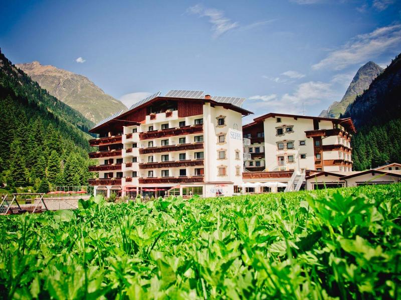 Mehrstöckiges Hotel in Berglandschaft mit grünem Feld und blauem Himmel im Hintergrund.