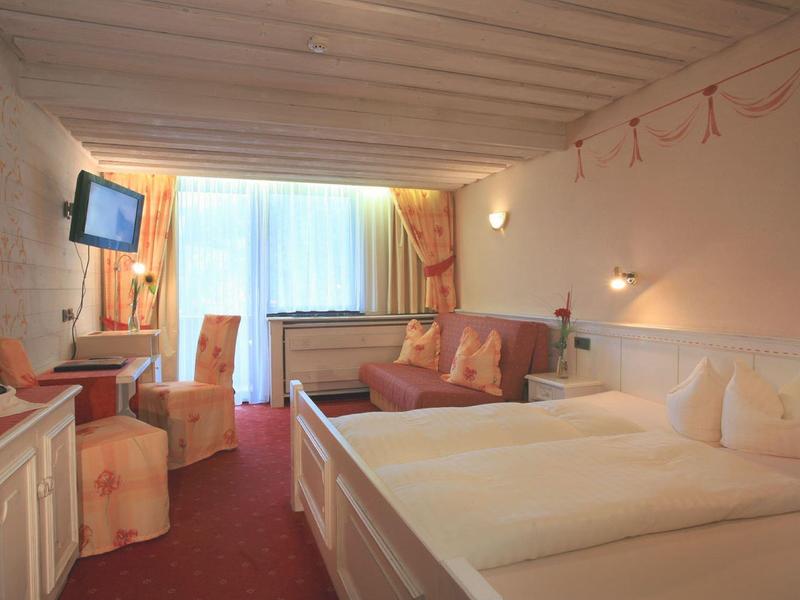 Gemütliches Hotelzimmer mit Doppelbett, Sofa, Tisch, Stühlen und Fernseher an der Wand.