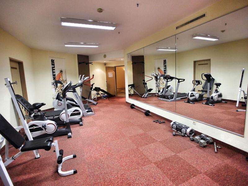 Kleiner Fitnessraum mit roten Teppichboden, Spiegelwand und verschiedenen Trainingsgeräten.