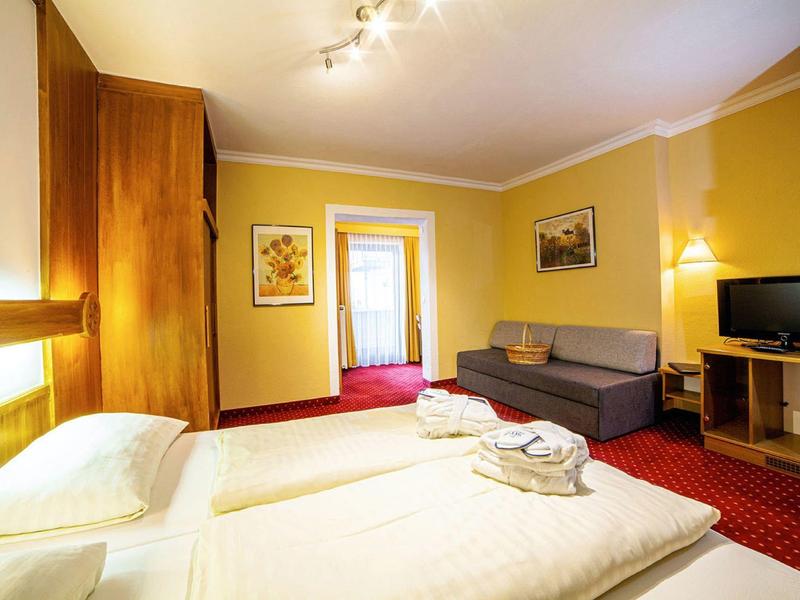 Gemütliches Hotelzimmer mit Doppelbett, Sofa, Fernseher und warmen Gelb- und Rottönen.